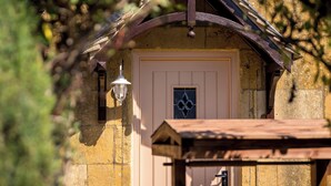 A rustic building with a wooden door, a small porch, and a lantern. - Broadway Scandi Chic Cottage (Broadway)