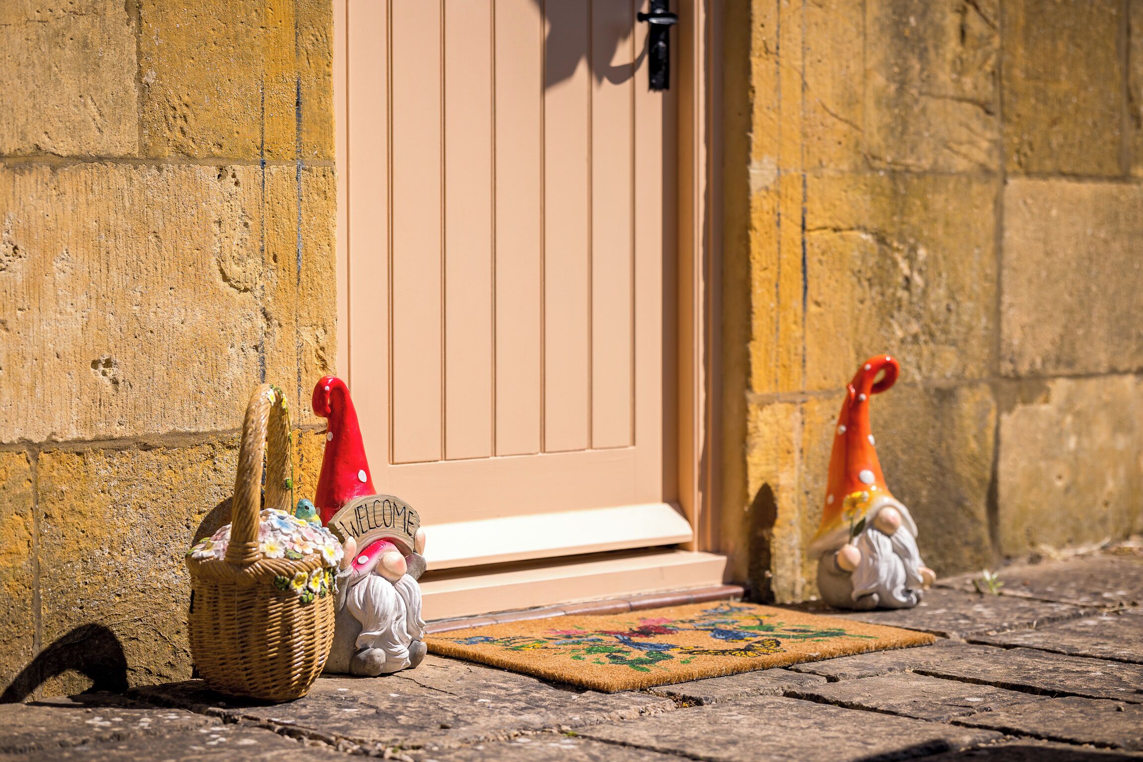 Una cesta de mimbre, un felpudo y dos figuritas de gnomos frente a una puerta.
