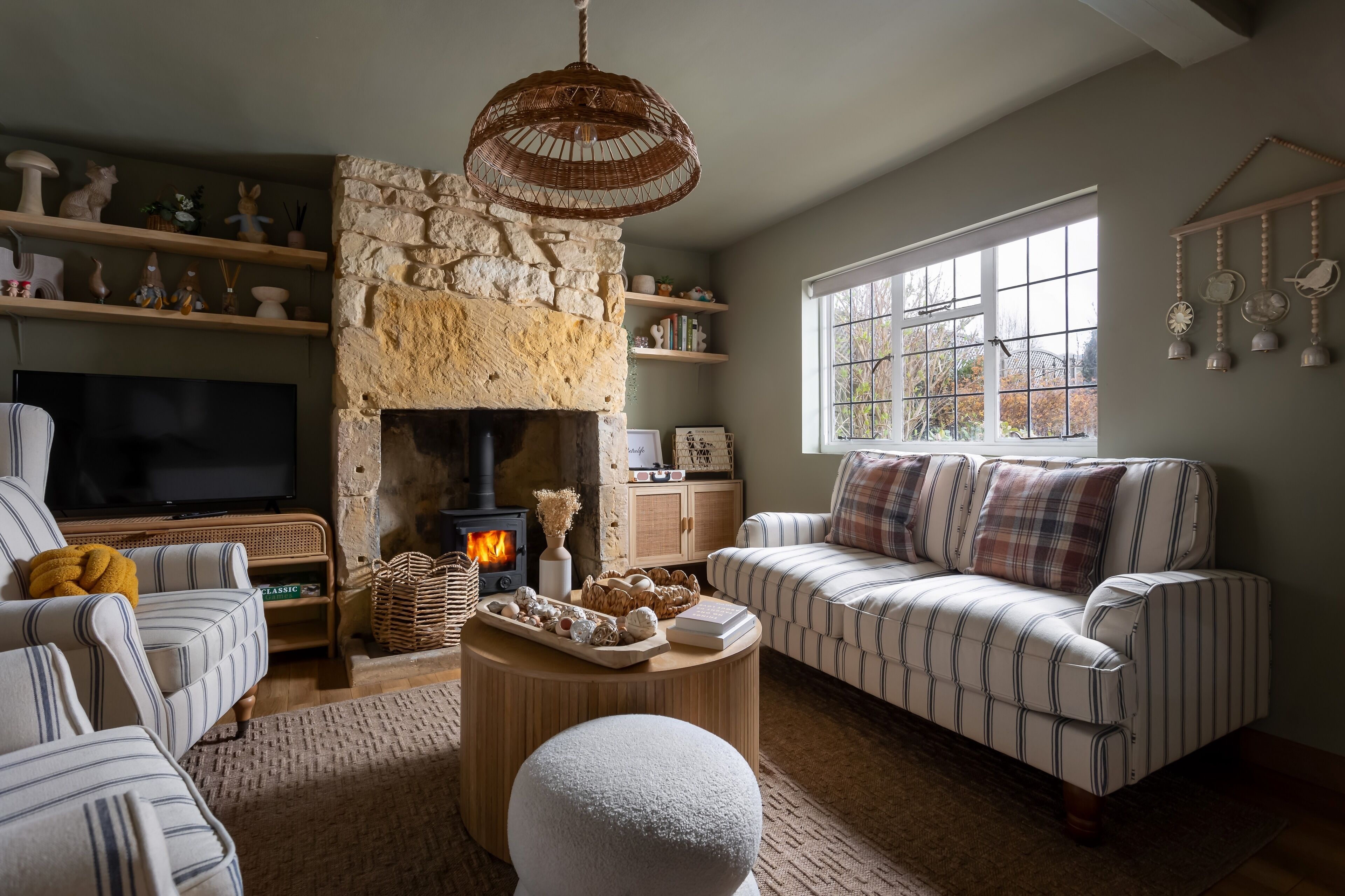 A cozy living room with a stone fireplace, striped sofas, a television, and decorative shelves.