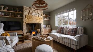 A cozy living room with a stone fireplace, striped sofas, a television, and decorative shelves.
