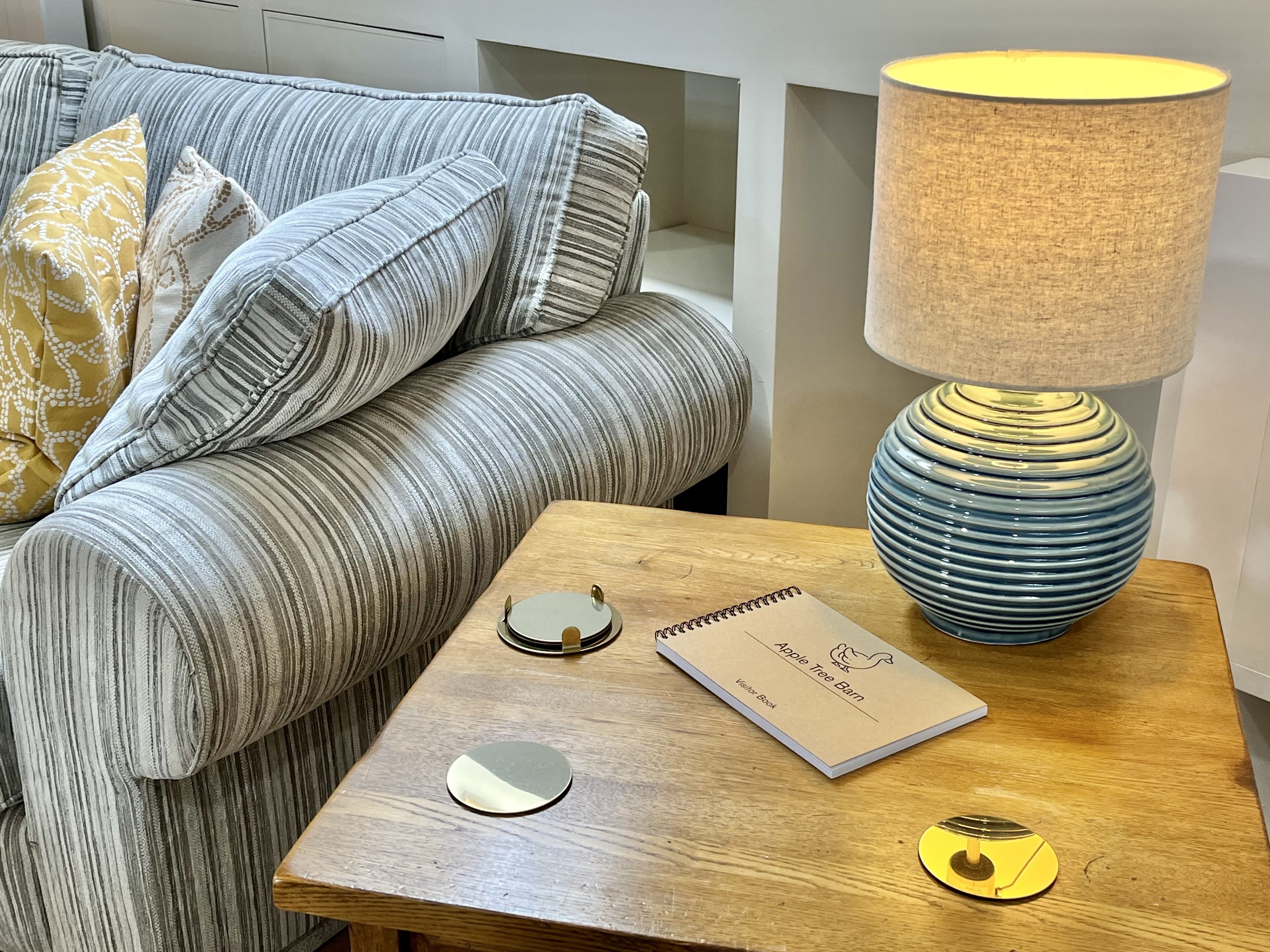 A modern living room with a striped sofa, a wooden side table, a lamp, a notebook, and a decorative plate.