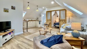 A spacious loft with a high ceiling, a cozy seating area with a sofa and armchair, a dining table, and a kitchen area with a window overlooking the city. - Apple Tree Barn by inspirestays.com - a cottage that sleeps 4 guests in 2 bedrooms (Walberton Green, nr Arundel)