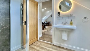 A modern bathroom with a glass shower enclosure, a wooden door, a white sink with a mirror, and a skylight above. - Apple Tree Barn by inspirestays.com - a cottage that sleeps 4 guests in 2 bedrooms (Walberton Green, nr Arundel)