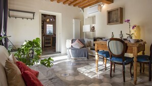 Uma sala de estar acolhedora com sofá, cadeiras, uma mesa de jantar e uma cozinha ao fundo.