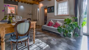 Um quarto acolhedor com uma mesa de jantar de madeira, um sofá com almofadas, uma janela grande e uma planta em vaso.