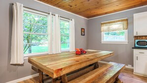 A kitchen with a wooden table and bench, two windows with curtains, a microwave, and a small toy car on the table.