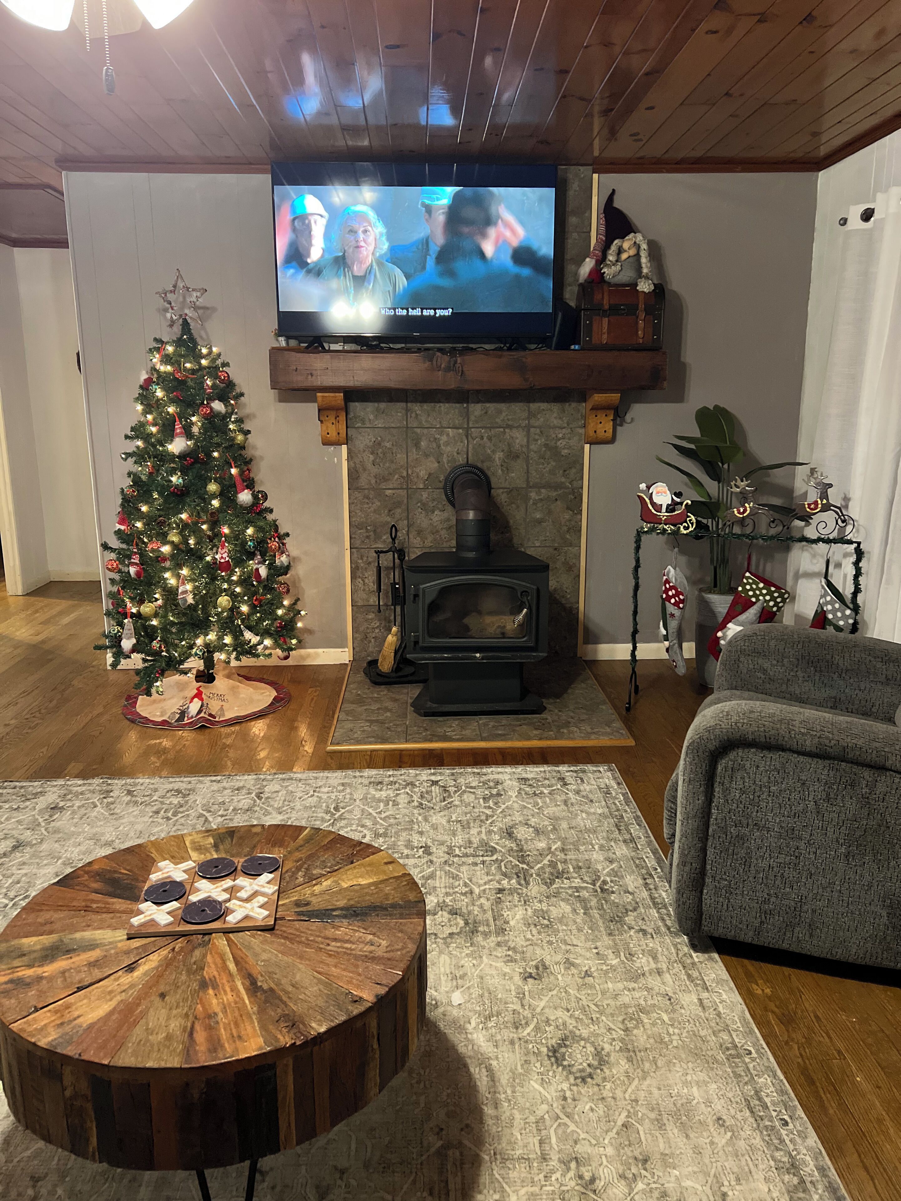 A cozy living room with a Christmas tree, a fireplace, a television, and a round coffee table.