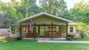 A single-story house with a porch, an American flag, and a welcome sign.