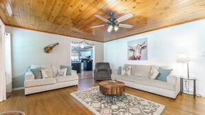 A spacious living room with wooden floors, two sofas, a coffee table, and a ceiling fan.