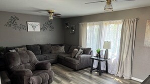 Un salon comprenant un canapé d’angle, une petite table avec une lampe et un ventilateur de plafond.