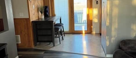 Een moderne woonkamer met een houten vloer, een donkere bank en een eethoek met een tafel en stoelen.