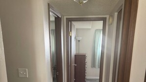 Un couloir doté d’un plancher en bois, d’un luminaire au plafond et d’une porte donnant sur une autre pièce.