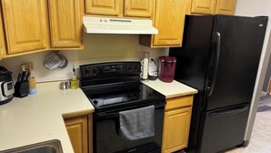 Une cuisine avec des meubles de rangement en bois, une cuisinière noire, un réfrigérateur noir et un plan de travail blanc.