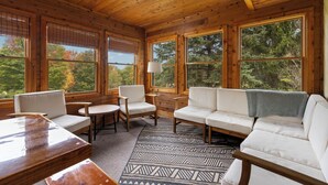 L’intérieur d’un chalet en bois comprend un canapé, des fauteuils, une table et de grandes fenêtres qui offrent une vue sur les arbres.