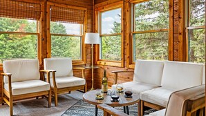L’intérieur d’un chalet en bois, avec un canapé, deux fauteuils, une table avec des boissons et une lampe.