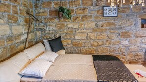 Um quarto aconchegante com parede de pedra, cama com roupa de cama estampada, uma planta pendente e um quadro na parede.