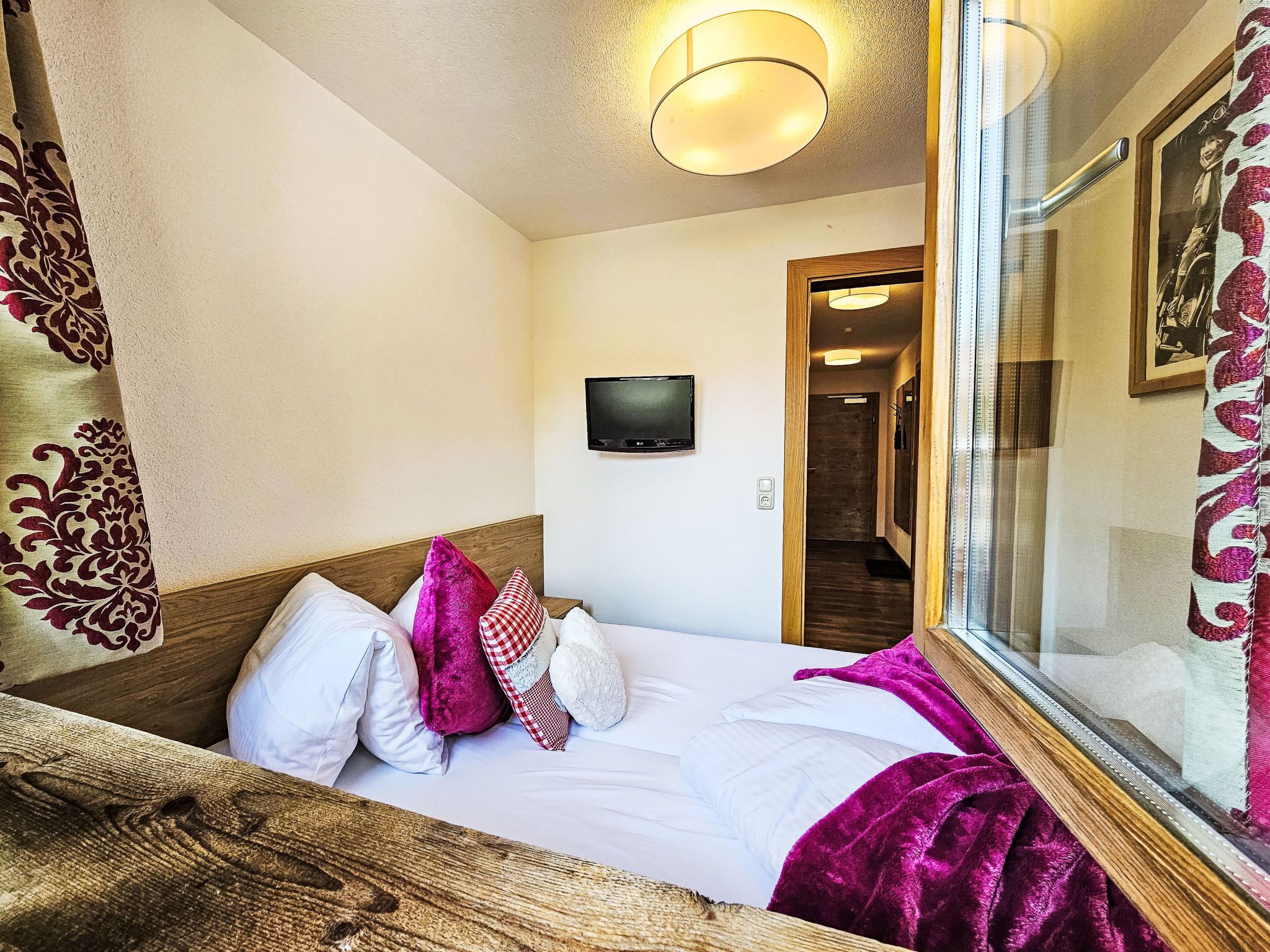 A hotel room with a bed, pillows, a television, and a mirror.