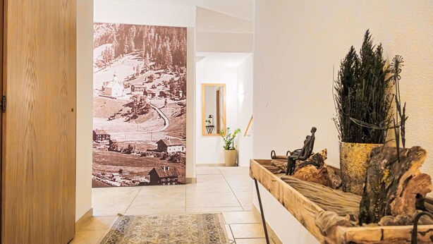 A hallway with a large vintage photograph, a wooden bench with decorative items, and a potted plant. - Panorama by Interhome (See)