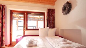 A double bed with white linens and towels, a wooden ceiling, and a window with curtains. - Panorama by Interhome (See)