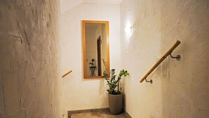 A narrow hallway with textured walls, a wooden door frame, a potted plant, and a wall-mounted towel rack.
