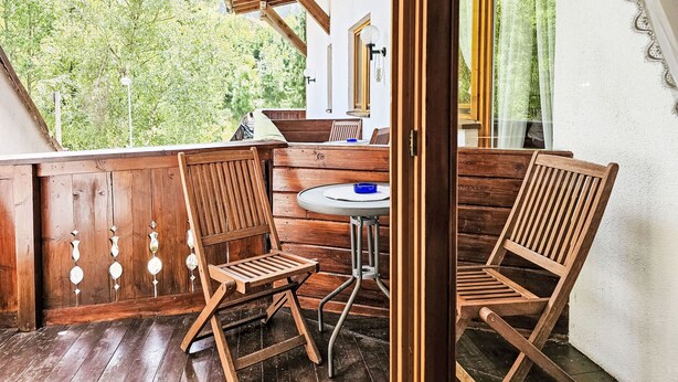 A wooden deck with two chairs and a small table, overlooking a forested area.