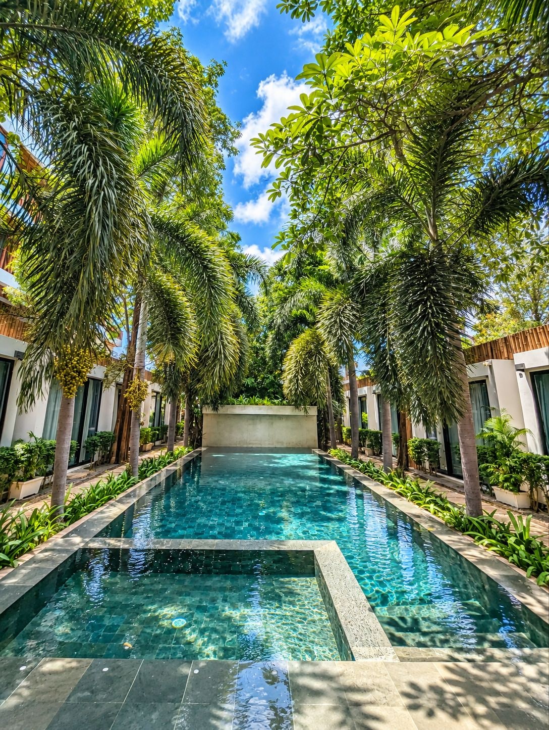 A rectangular pool with clear water, surrounded by lush greenery and modern architecture.