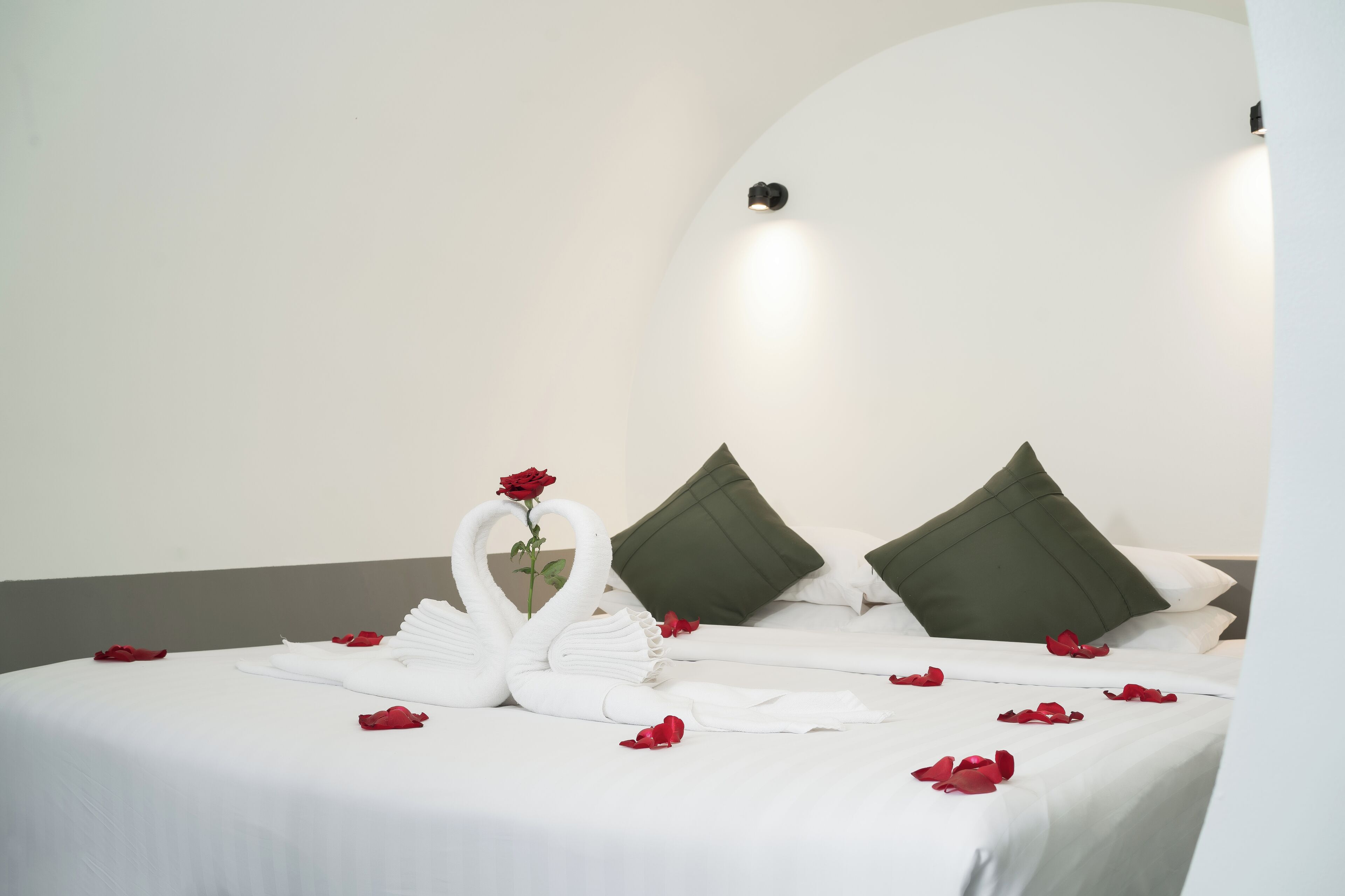 Ein ordentlich bezogenes Bett mit weißen Leinentüchern, grünen Kissen und roten Rosenblüten.