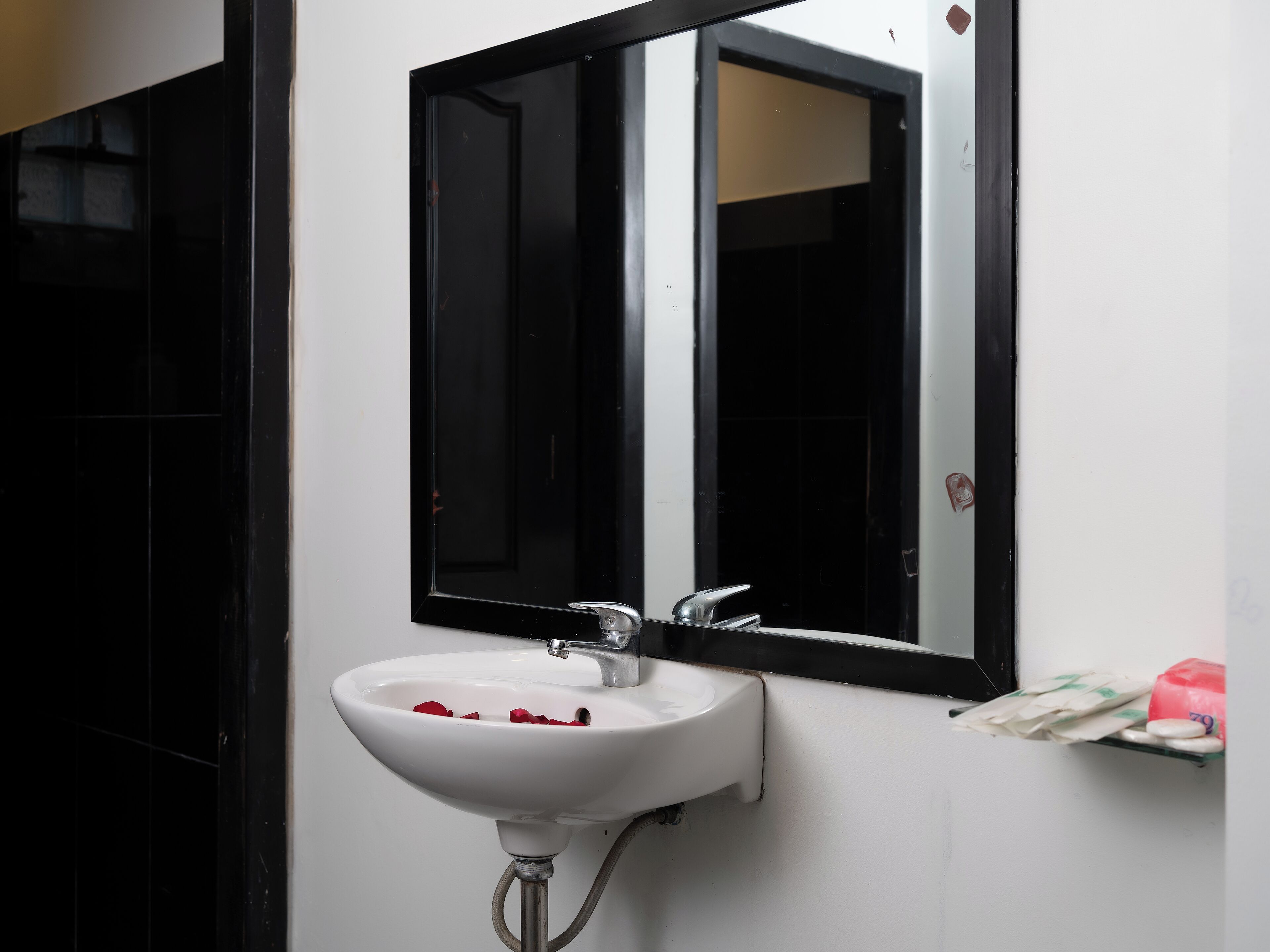 A bathroom with a white sink, black mirror, and a small shelf with toiletries.