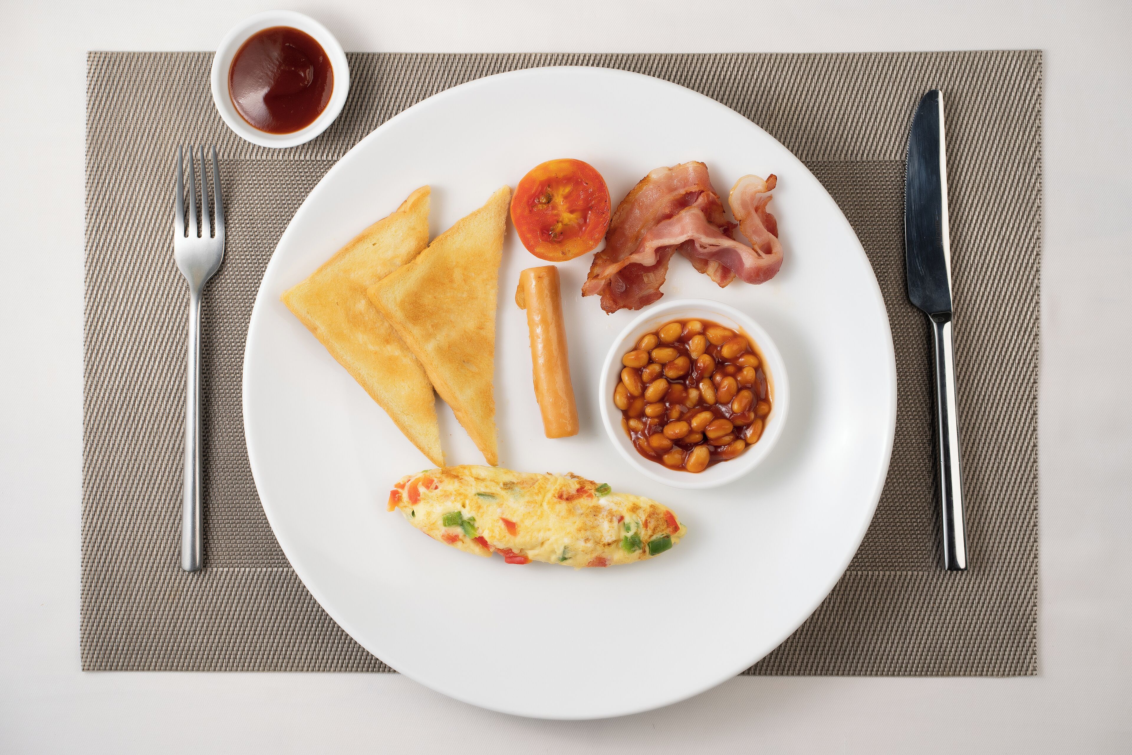 Un plato con tostadas, tocino, frijoles, tomate y una tortilla.
