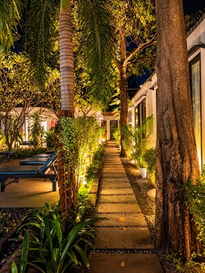 Un chemin bordé d’arbres et de plantes qui mène à un bâtiment au design moderne.