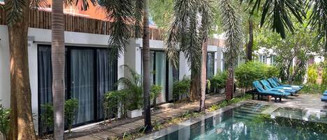 A pool area with lounge chairs, palm trees, and a building with large windows.