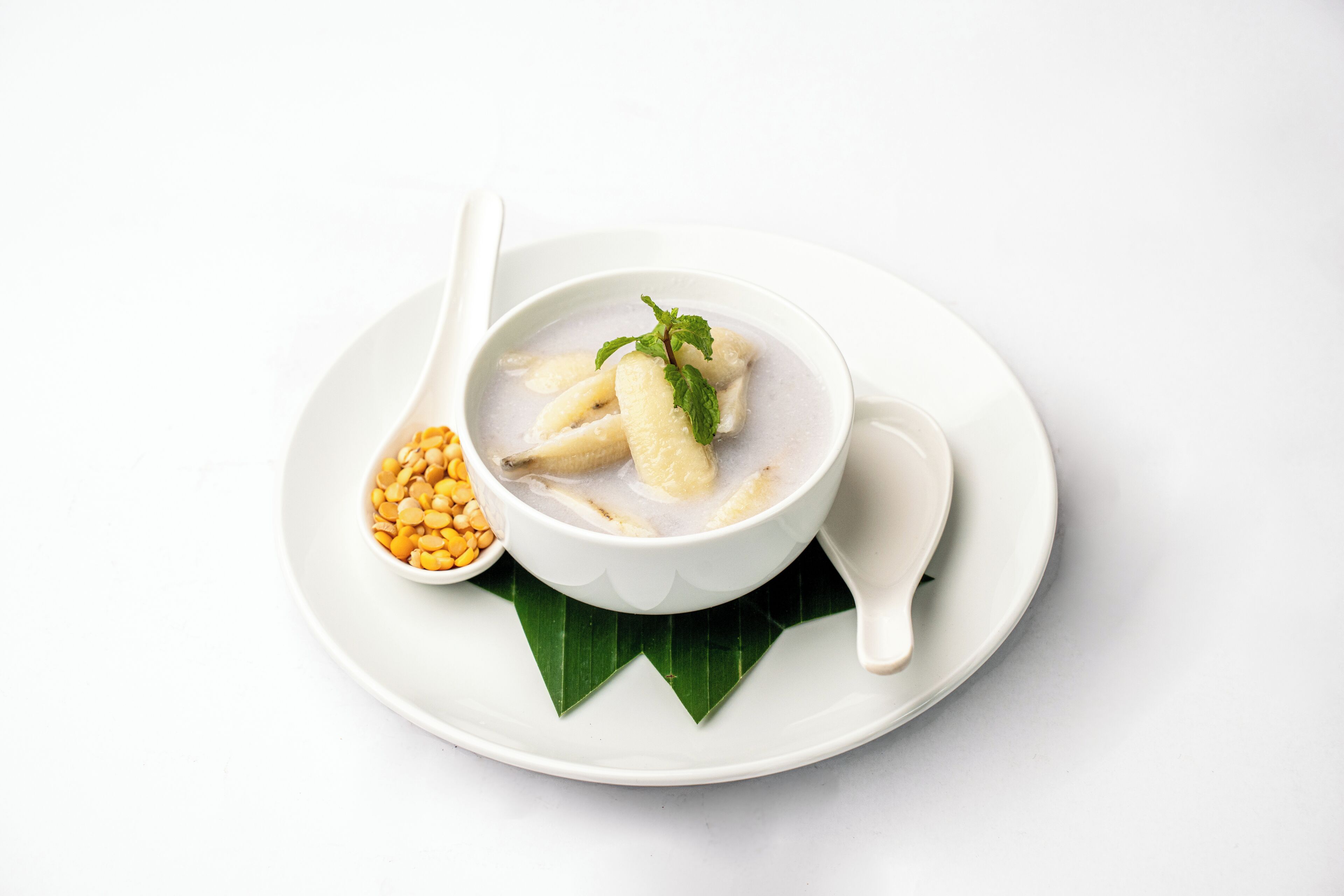 A bowl of soup with noodles and a spoon on a white plate.