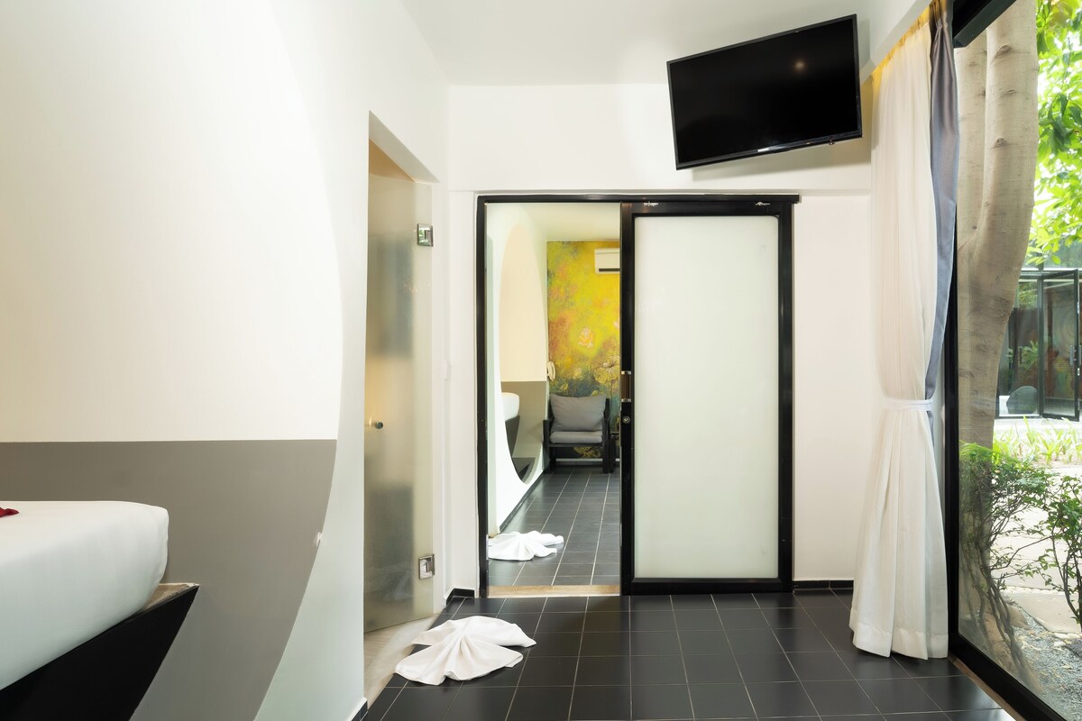A modern hotel room with a bed, a TV, and a sliding door leading to a bathroom.