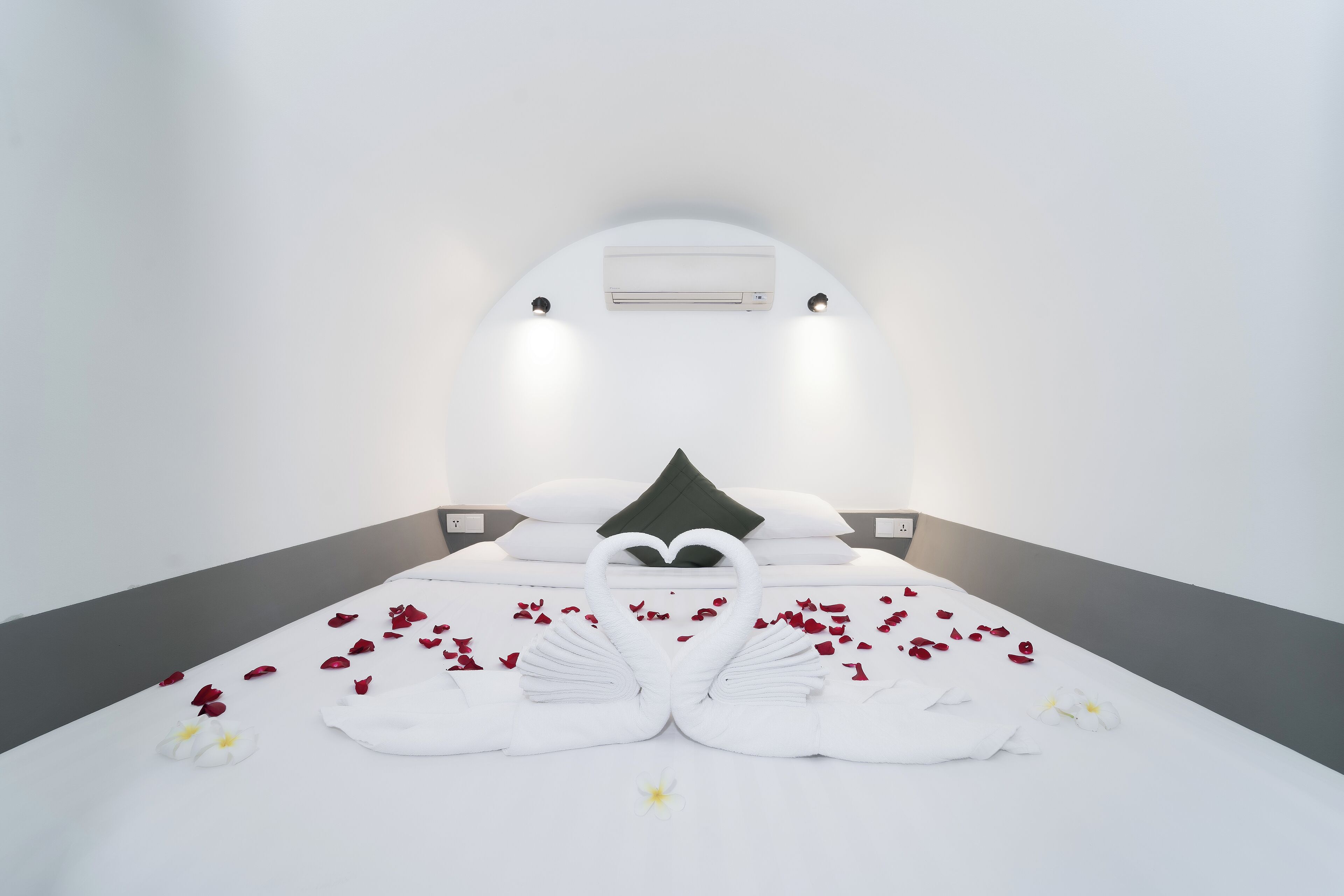 A modern hotel room with a bed, white walls, and a ceiling-mounted air conditioner.