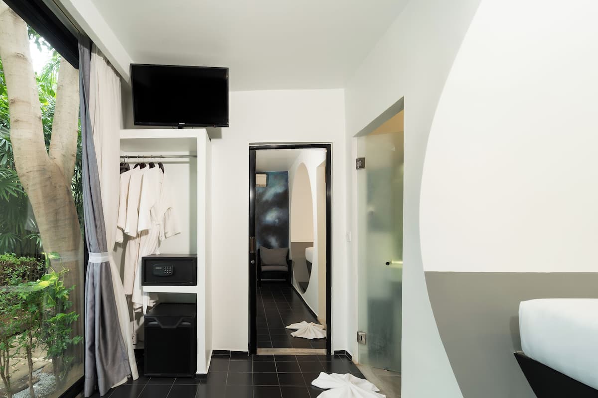 Quarto de hotel moderno com uma grande janela, TV de tela plana, closet espaçoso e banheiro com porta de vidro.