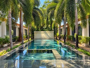 A rectangular swimming pool with clear water, surrounded by palm trees and greenery, with a modern building in the background. - Tunnel Urban Retreat (Siem Reap)
