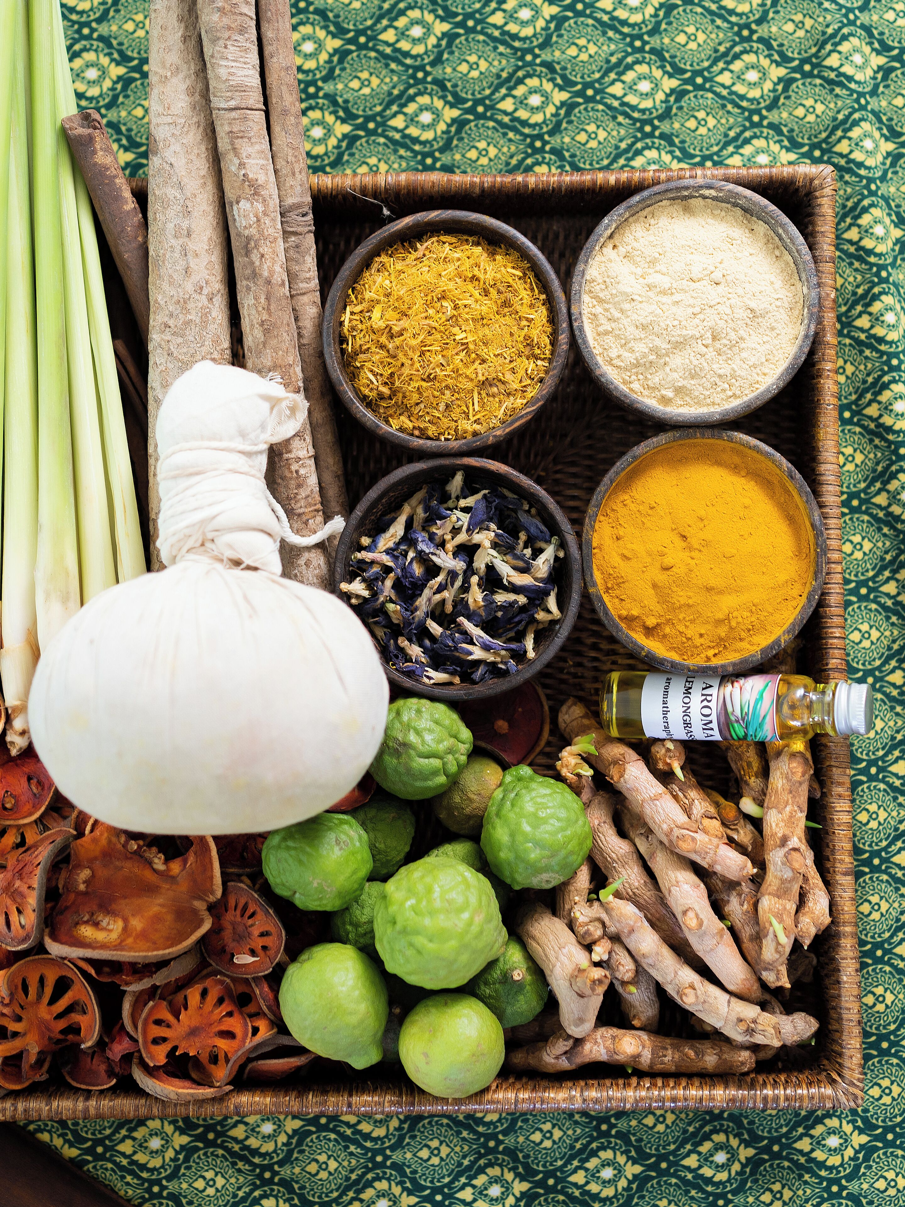 Una bandeja con diversas especias y hierbas, incluyendo cúrcuma, jengibre y hierba de limón, junto con frutas y verduras secas.