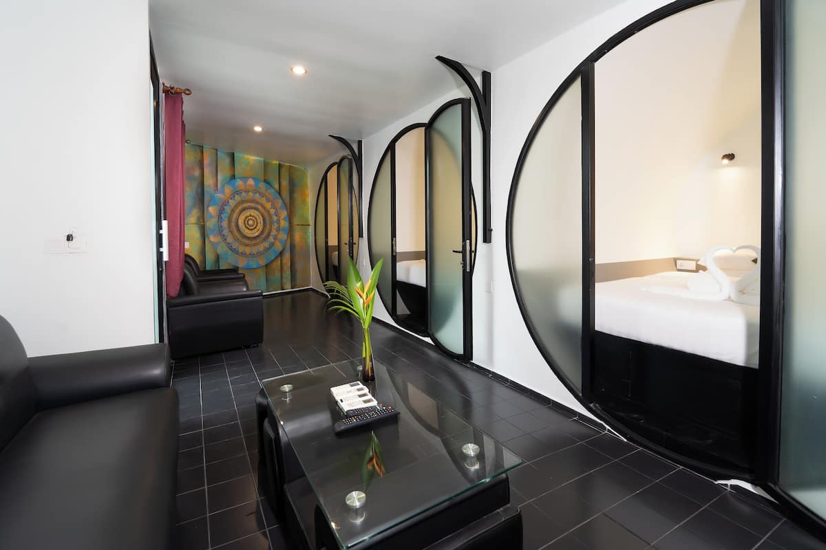 Quarto de hotel moderno com divisória de vidro, uma cama, secretária com controle remoto e um objeto decorativo na parede.
