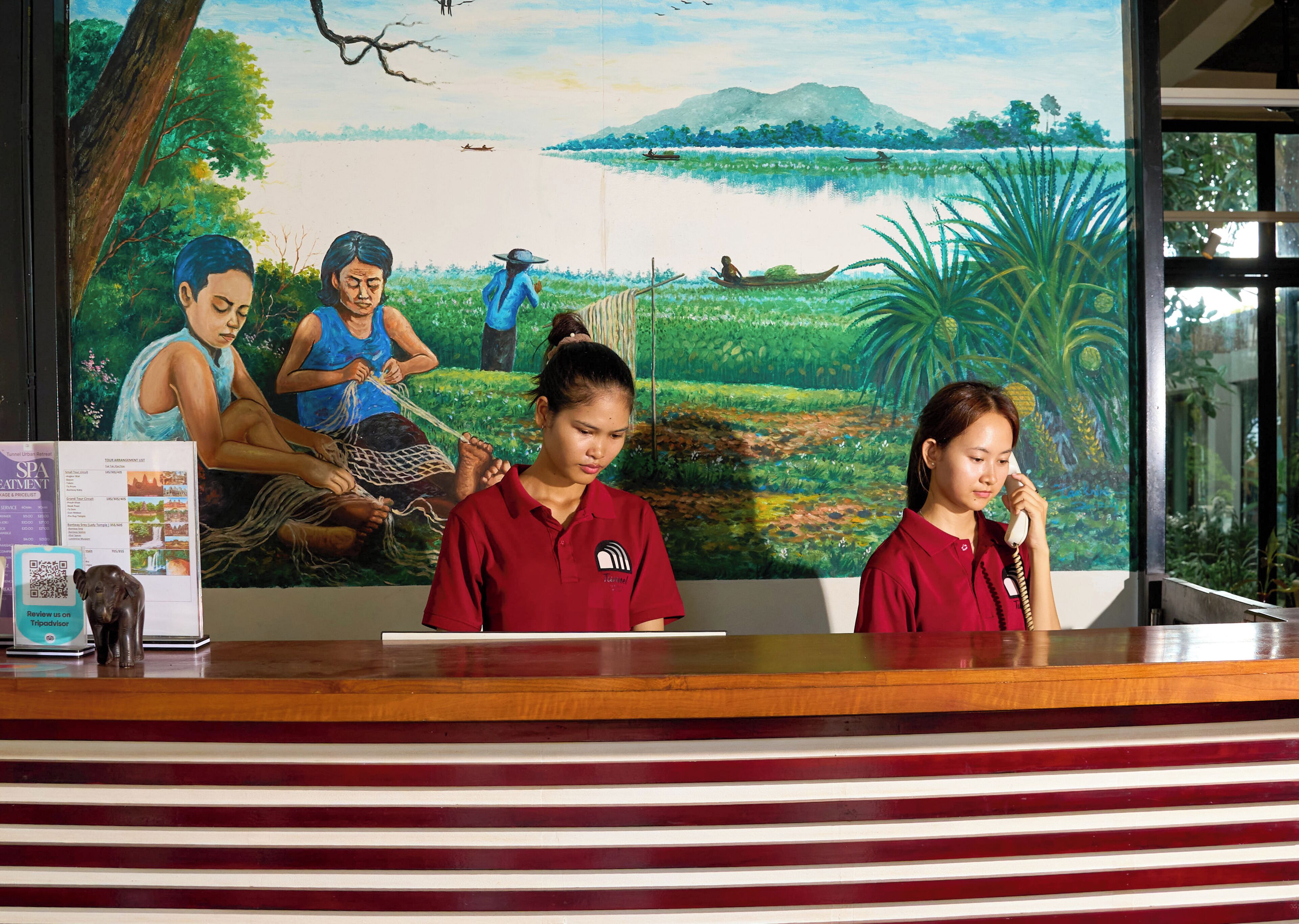 Una recepción con un mural que representa un paisaje tropical, una barra de madera y un cartel informativo enmarcado.
