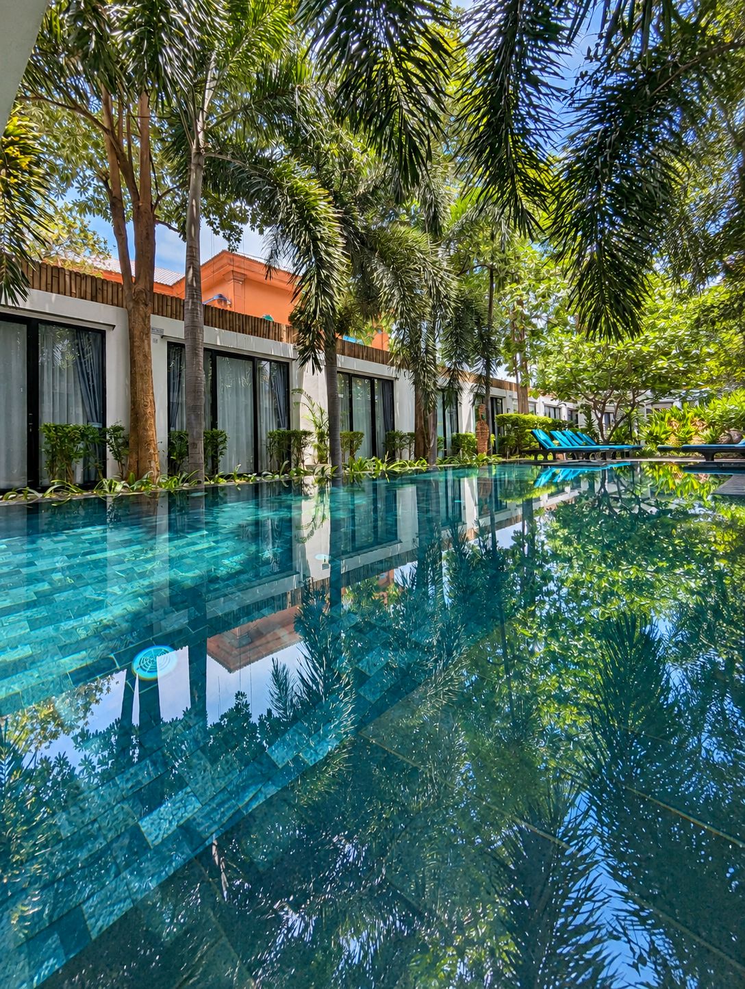 Una piscina cristalina rodeada de palmeras y edificios modernos con ventanales amplios.