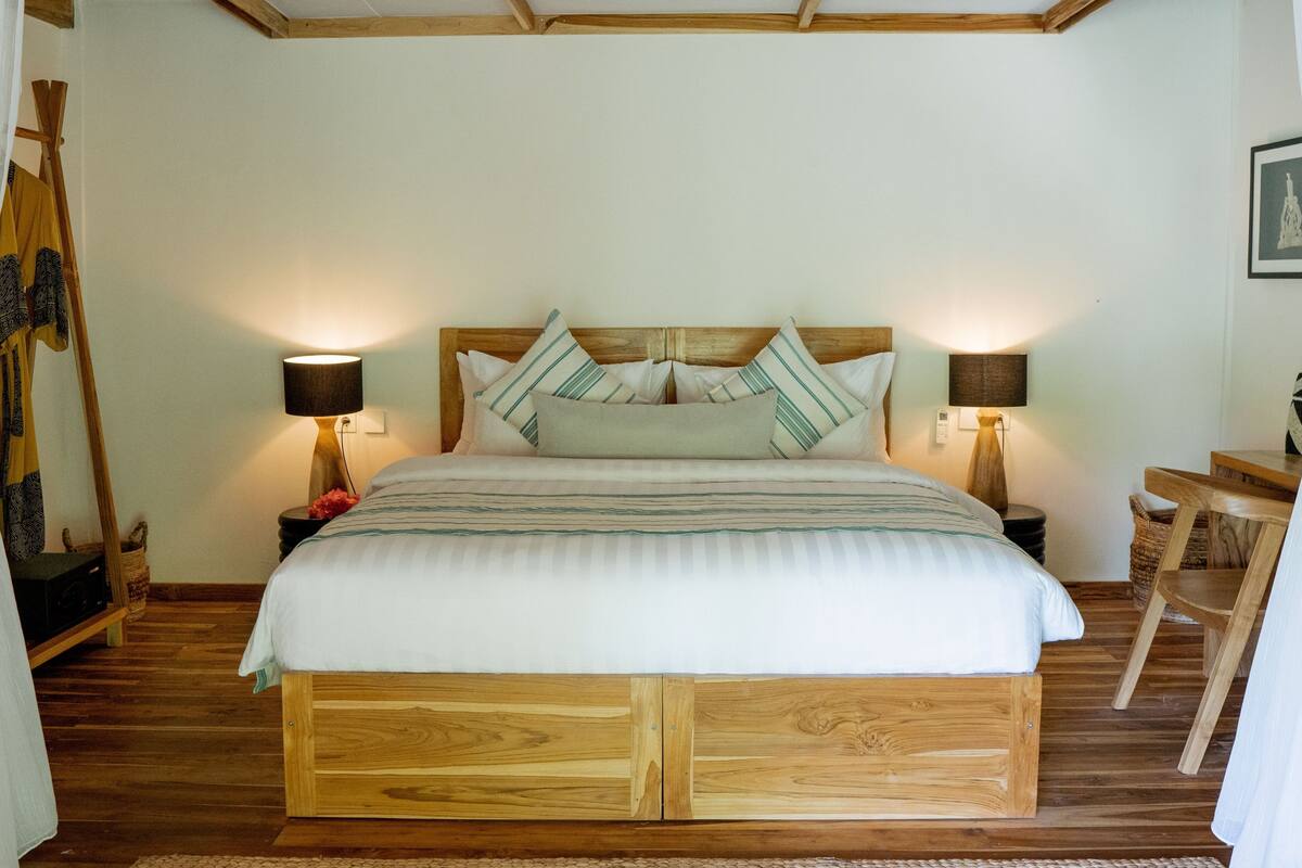 Una cama de madera con cabecera, dos lámparas de noche y una mesita de noche con lámpara.