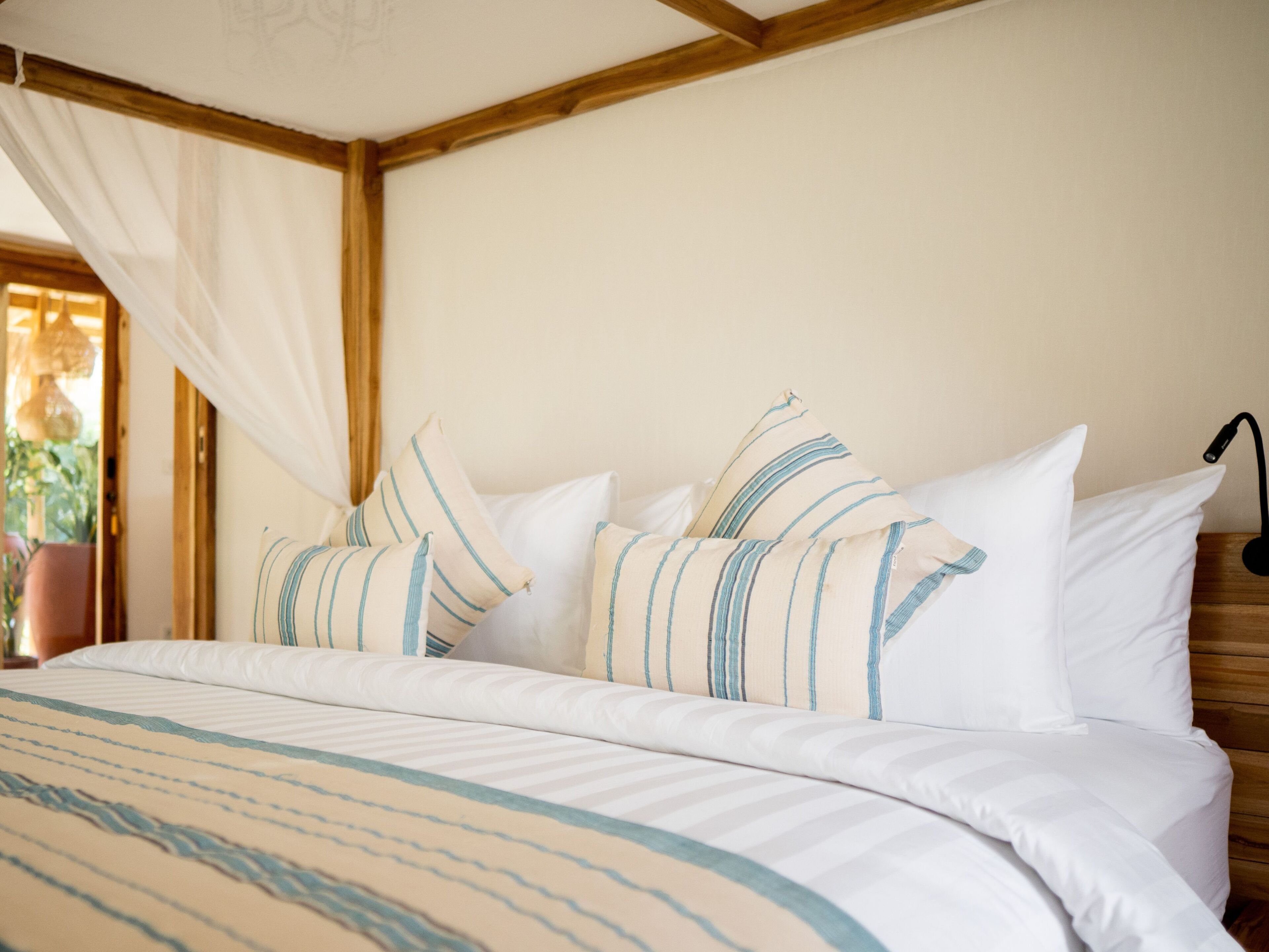 Una cama con ropa de cama a rayas, dosel y lámpara de noche.