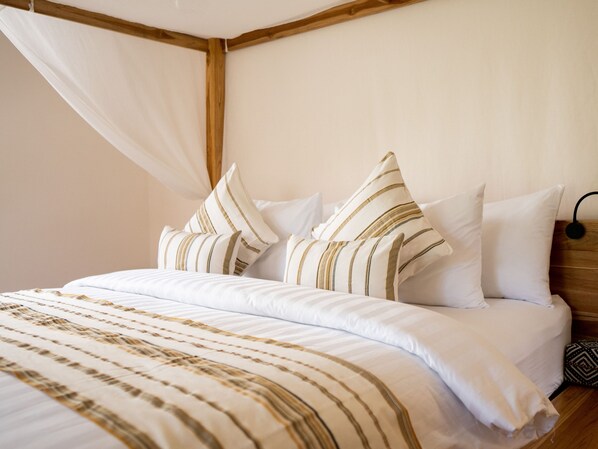Una cama bien hecha con ropa de cama a rayas y almohadas, cabecera de madera y dosel blanco.