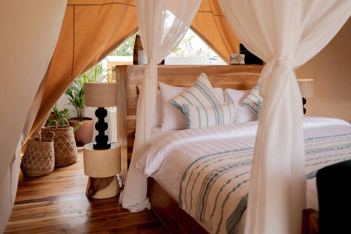 Un dormitorio con cama a dosel, cabecera de madera, lámparas de noche y cestas tejidas.
