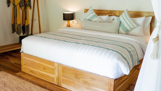 A neatly made bed with a wooden frame, white bedding with green stripes, and a bedside lamp. - Dejama Glamping Resort Lombok (Mertak)