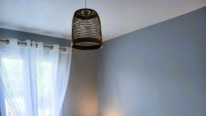 A bedroom with a bed, a bedside table, a lamp, and a window with curtains. - The P'tit Jard near the beach (Jard-sur-Mer)