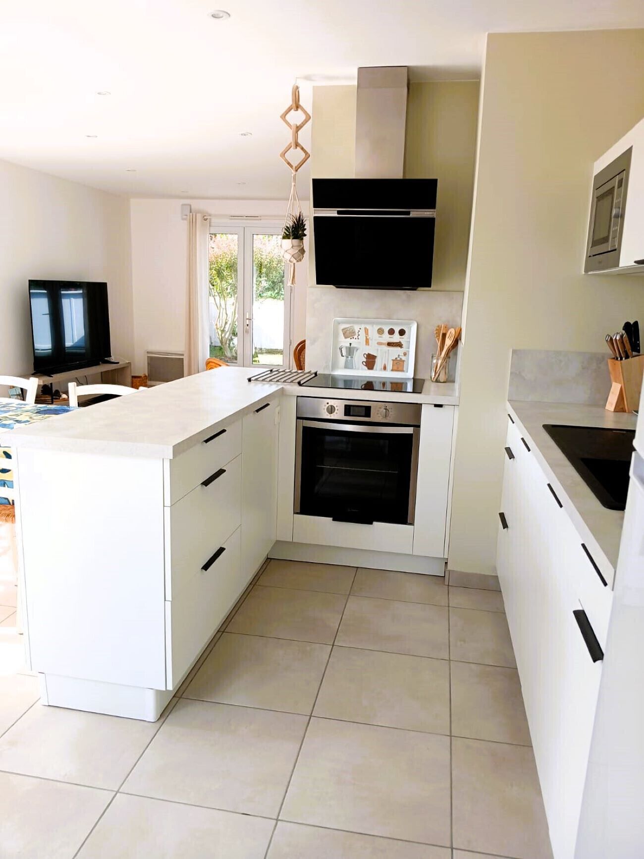 A modern kitchen with white cabinetry, a central island, a built-in oven, and a flat-screen TV.