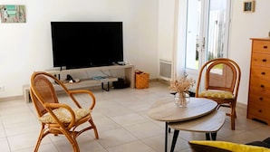 A living room with a flat-screen TV, wicker chairs, a round table with a vase, and a dark sofa. - The P'tit Jard near the beach (Jard-sur-Mer)