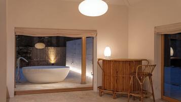 A modern bathroom with a freestanding bathtub, a wooden chair, and a glass shower enclosure.