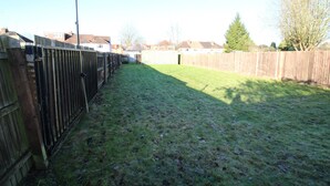 A fenced backyard with a grassy lawn, a wooden fence, and a tall streetlight. - Bungalow - Sleeps 8 - Pets-Enclosed Garden-Parking (Birmingham)